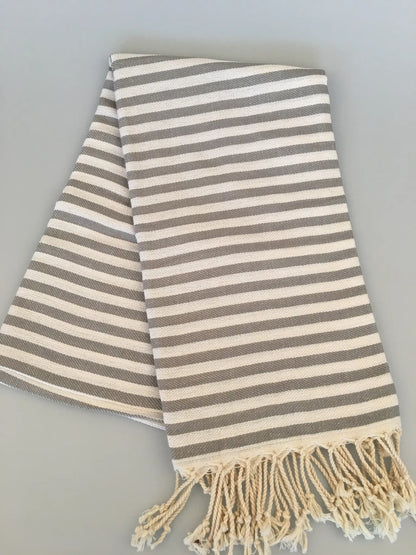 Gray and cream striped Turkish towel with fringed edges, neatly folded on a light gray background.