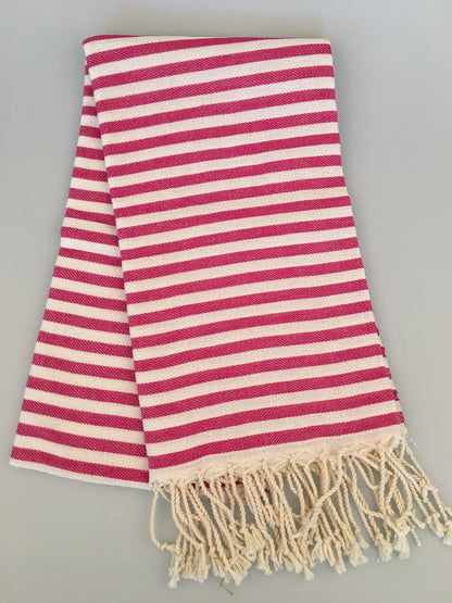 "Striped Turkish towel in pink and white with tassels at one end, folded flat on a light background."
