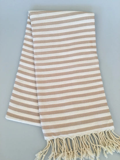 "Beige and cream striped Turkish towel with fringed edges, folded flat on a light gray background."