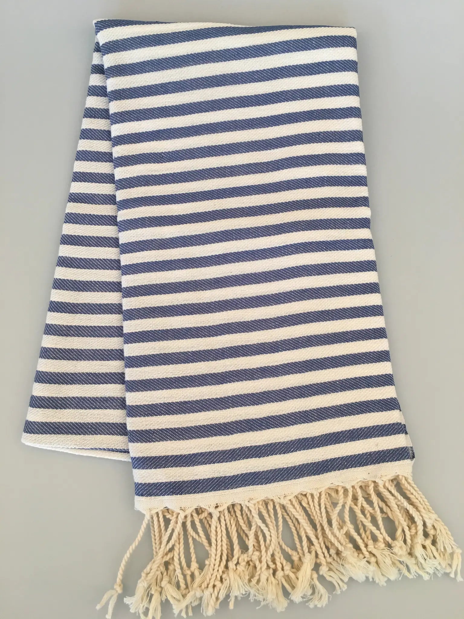"Blue and white striped Turkish towel with fringed edges, folded flat on a light background."