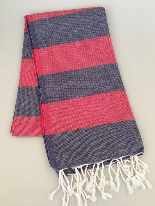 "Pinara Turkish towel peshtamal in navy blue with red stripes and white fringes, folded on a light surface."