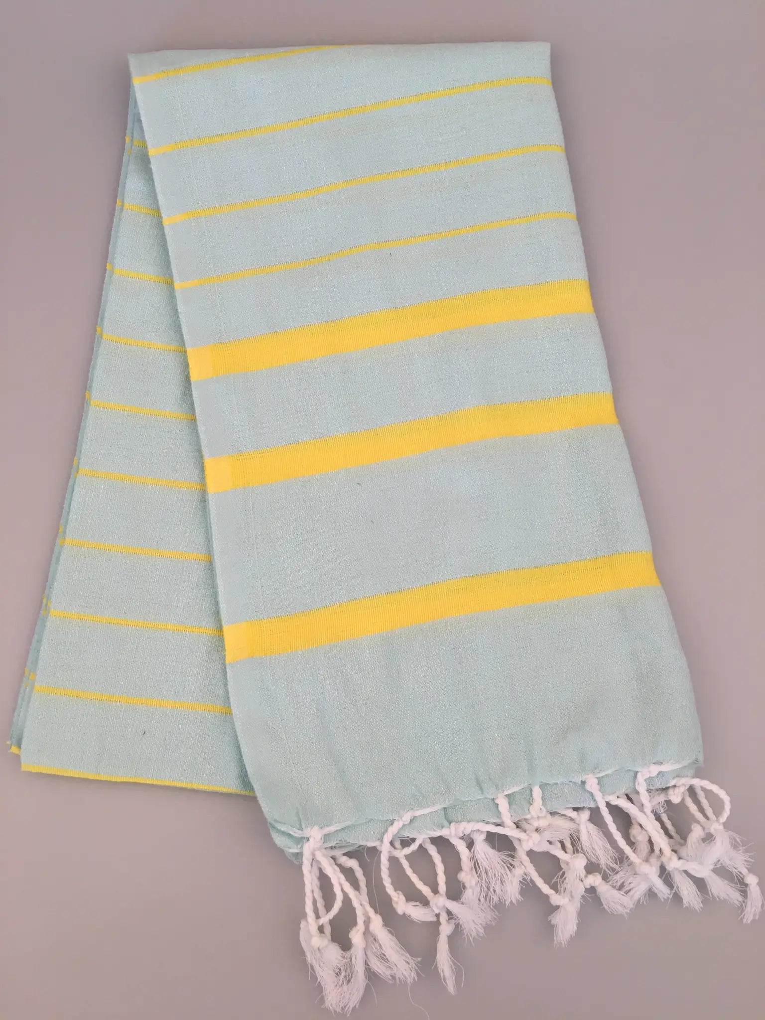 Light blue Turkish towel peshtemal with yellow stripes and white fringes, laid flat on a gray background.