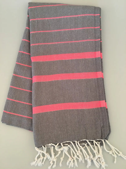 "Gray Turkish towel with pink stripes and white fringes, folded on a light surface"