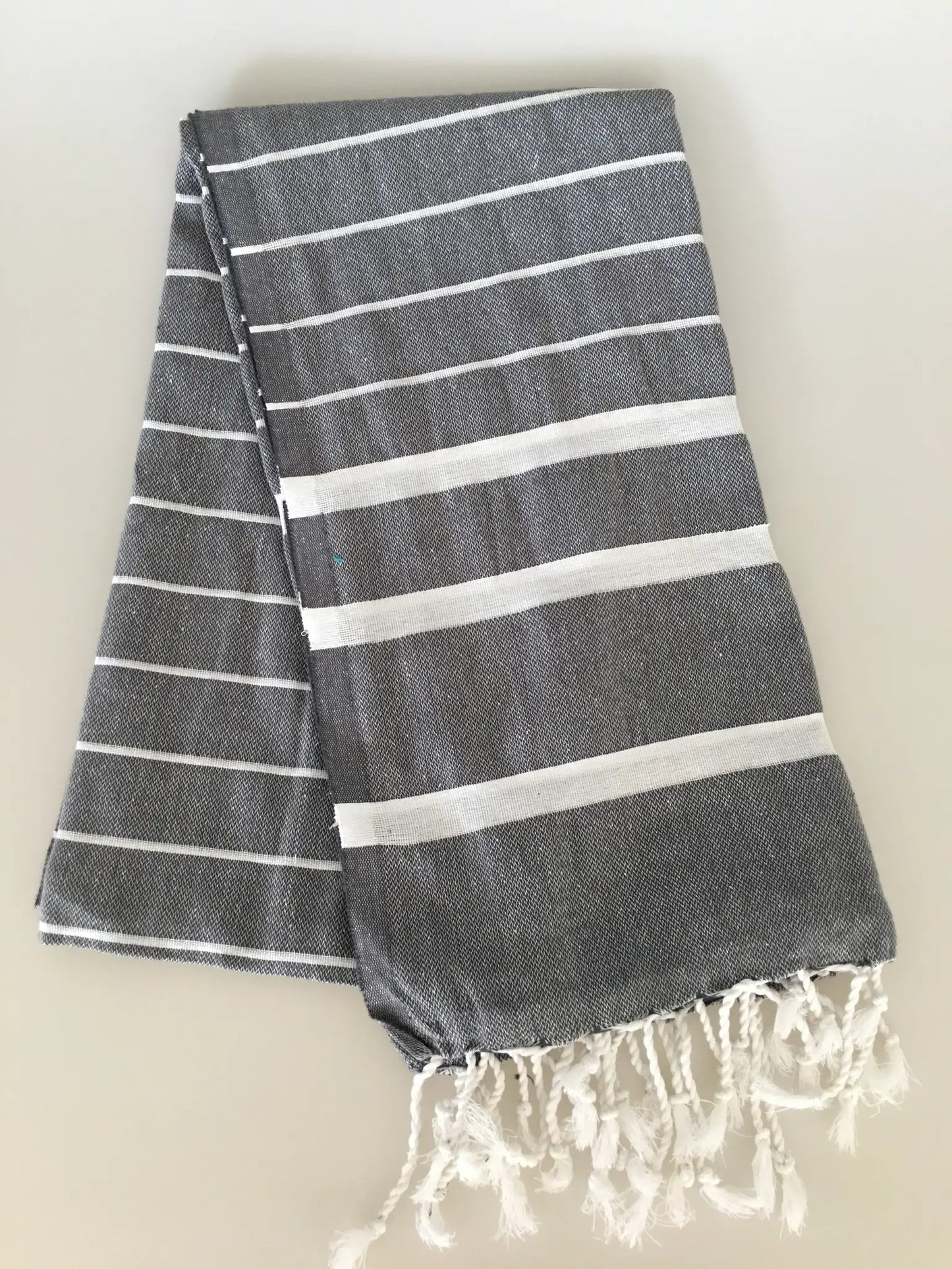 "Gray Turkish towel peshtemal with white stripes and fringed edges, neatly folded on a light background."