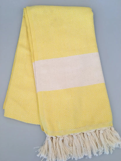 Yellow Turkish towel peshtemal with a white stripe and fringed edges, featuring a herringbone pattern.