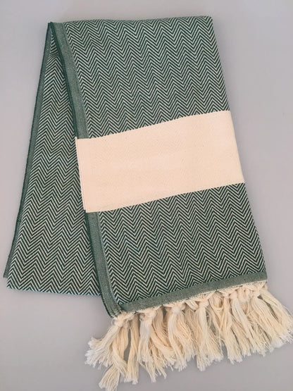 Green and white chevron-patterned Turkish towel with a cream-colored band and fringed edges, laid flat on a light background.