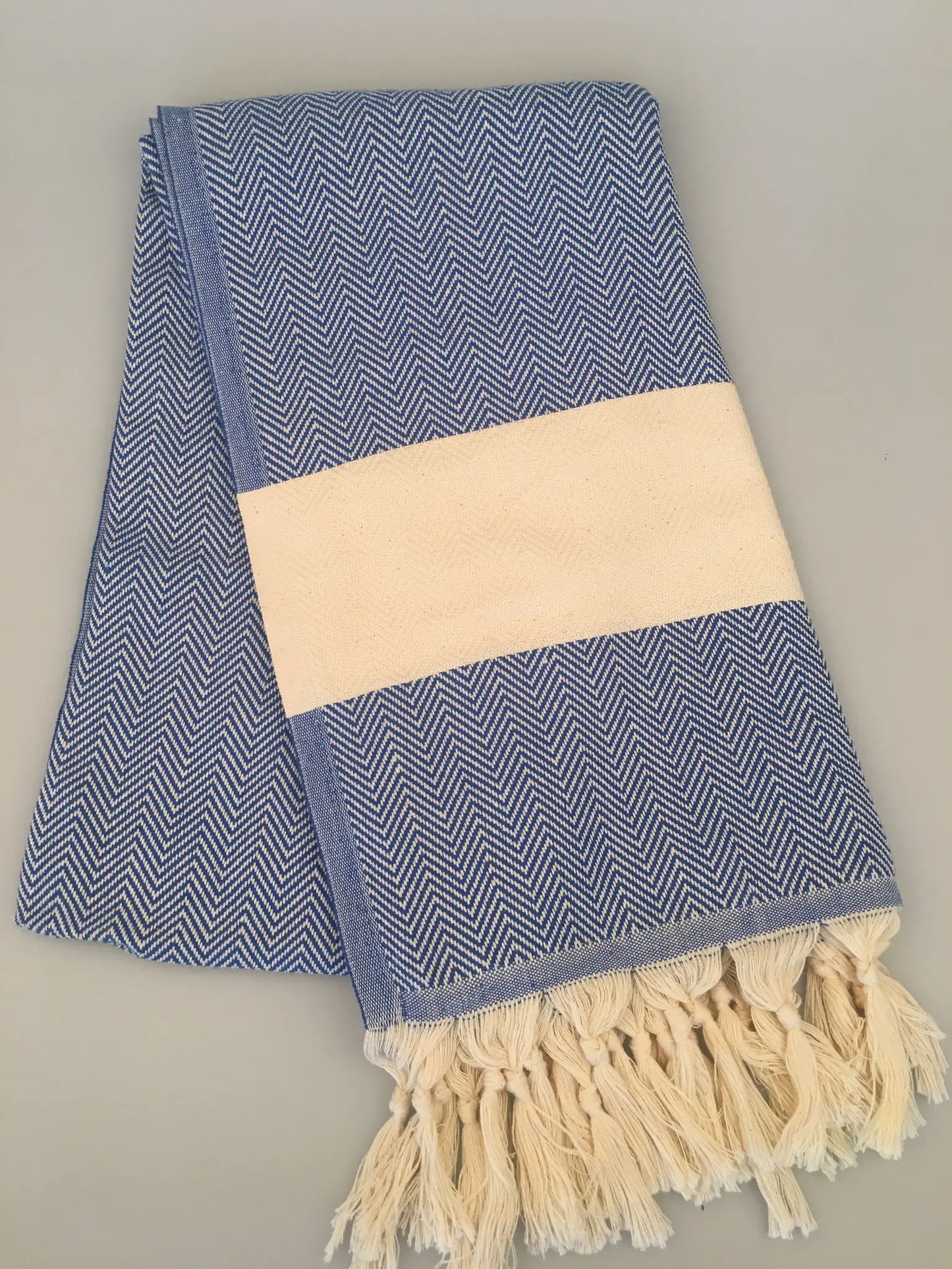 Blue and white chevron-patterned Turkish towel with cream-colored band and fringed edges, folded on a light background.