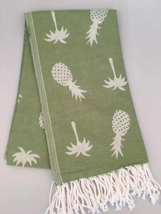 Green Turkish towel featuring white pineapple jacquard pattern and fringed edges, laid flat on a light background.