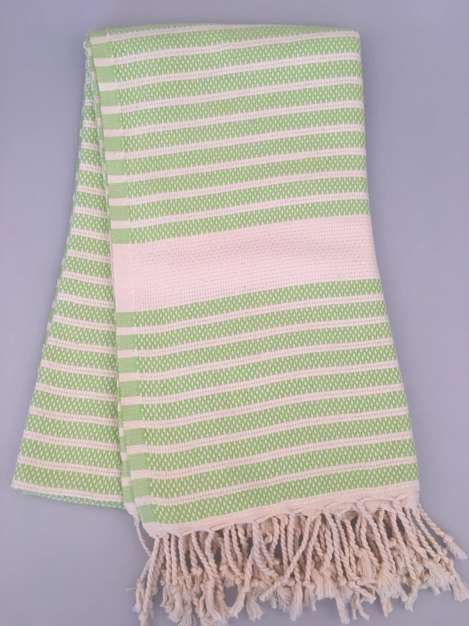 Green and white striped Hittite Turkish towel with fringed edges, folded on a light gray background.