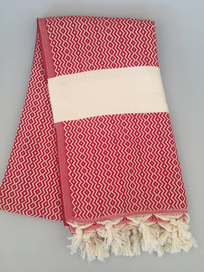 Red and white patterned Turkish towel with fringed edges, folded neatly, showcasing a textured design.