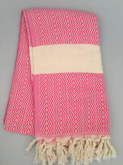 "Pink and white Turkish towel with zigzag pattern and fringed edges, folded view on light background."