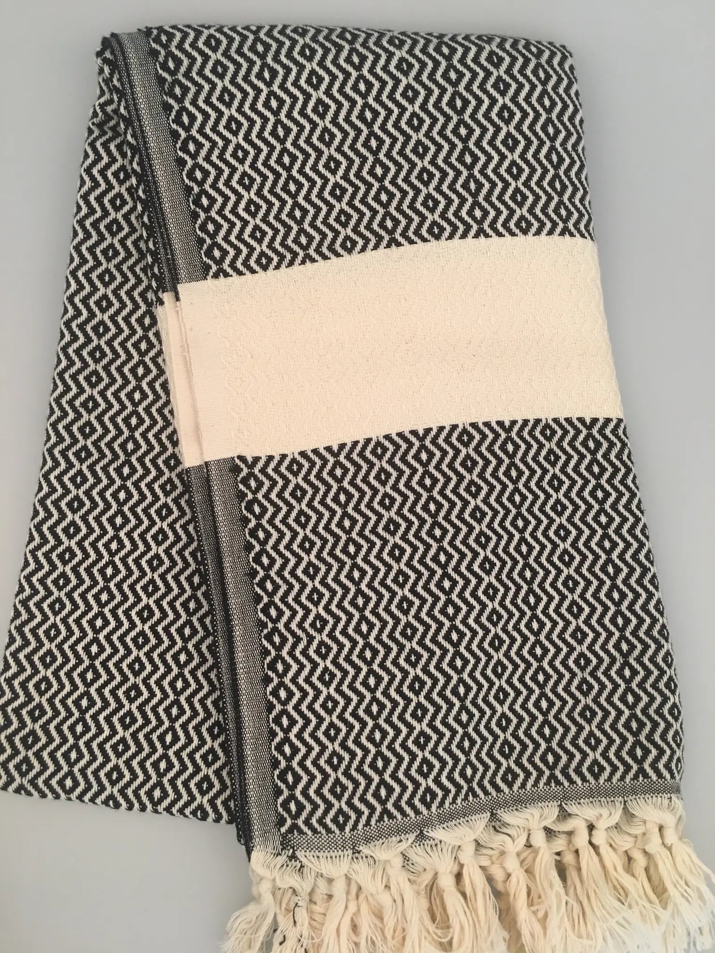 "Black and white patterned Turkish towel with cream stripe and fringed edges, folded neatly."