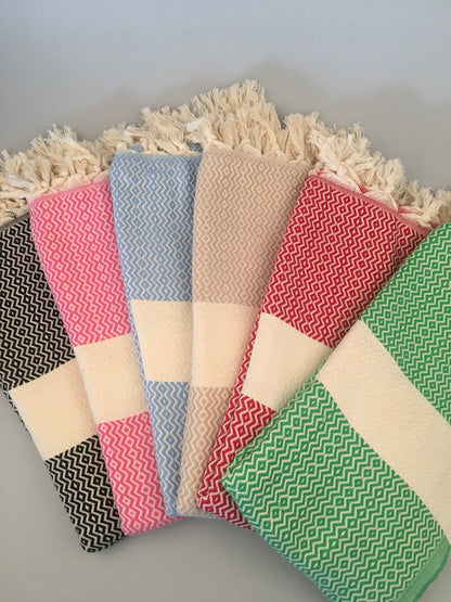 "Set of five Turkish towels in pink, blue, beige, red, and green with zigzag patterns and fringed edges, laid flat."