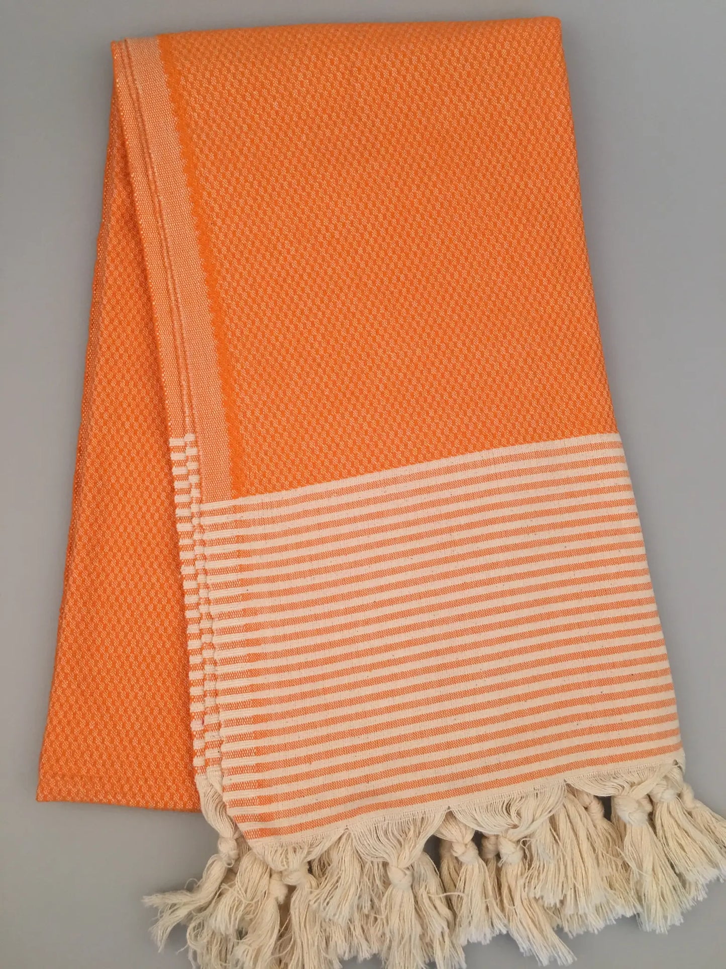 Orange Turkish towel peshtemal with textured weave, featuring a striped cream border and fringed edges, laid flat.