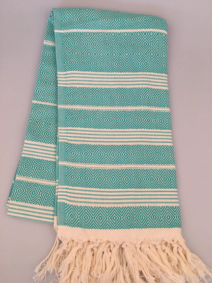 "Turquoise Turkish towel with diamond patterns and white stripes, fringed edges, laid flat on a neutral background."