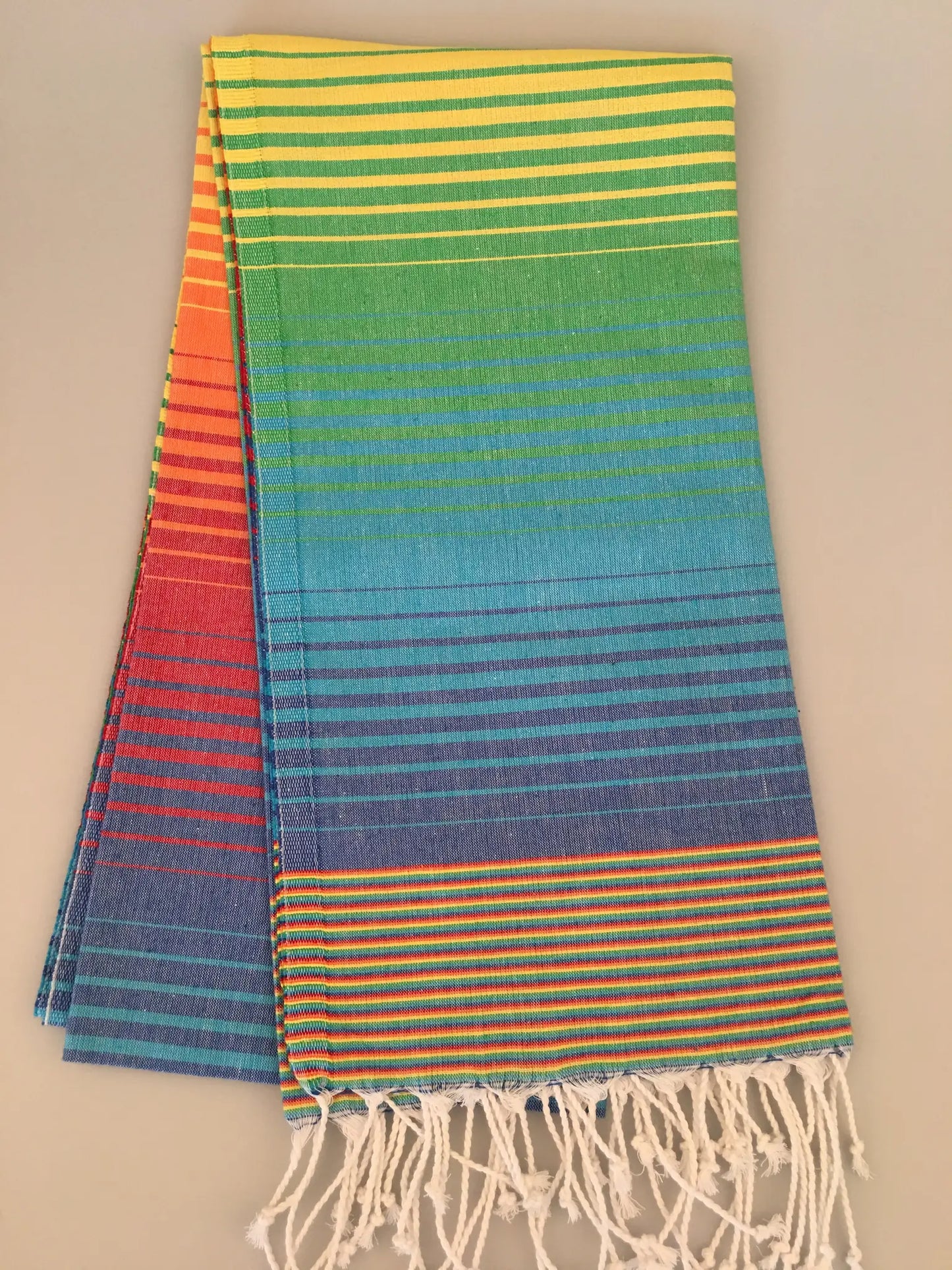 "Striped Turkish towel in vibrant colors of red, orange, yellow, green, blue, and purple, with fringed edges."