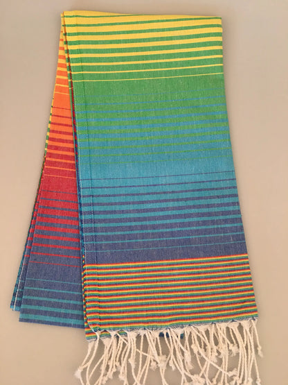 "Striped Turkish towel in vibrant colors of red, orange, yellow, green, blue, and purple, with fringed edges."