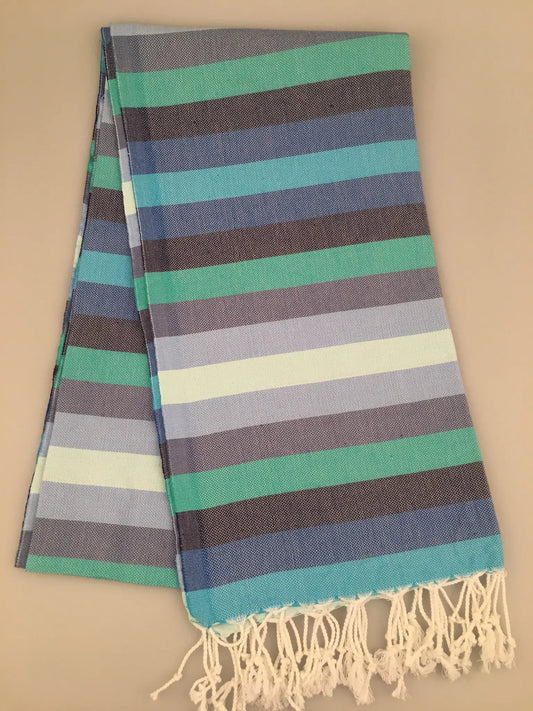 "Turquoise, blue, and gray striped Turkish towel with fringed edges, folded on a light background."
