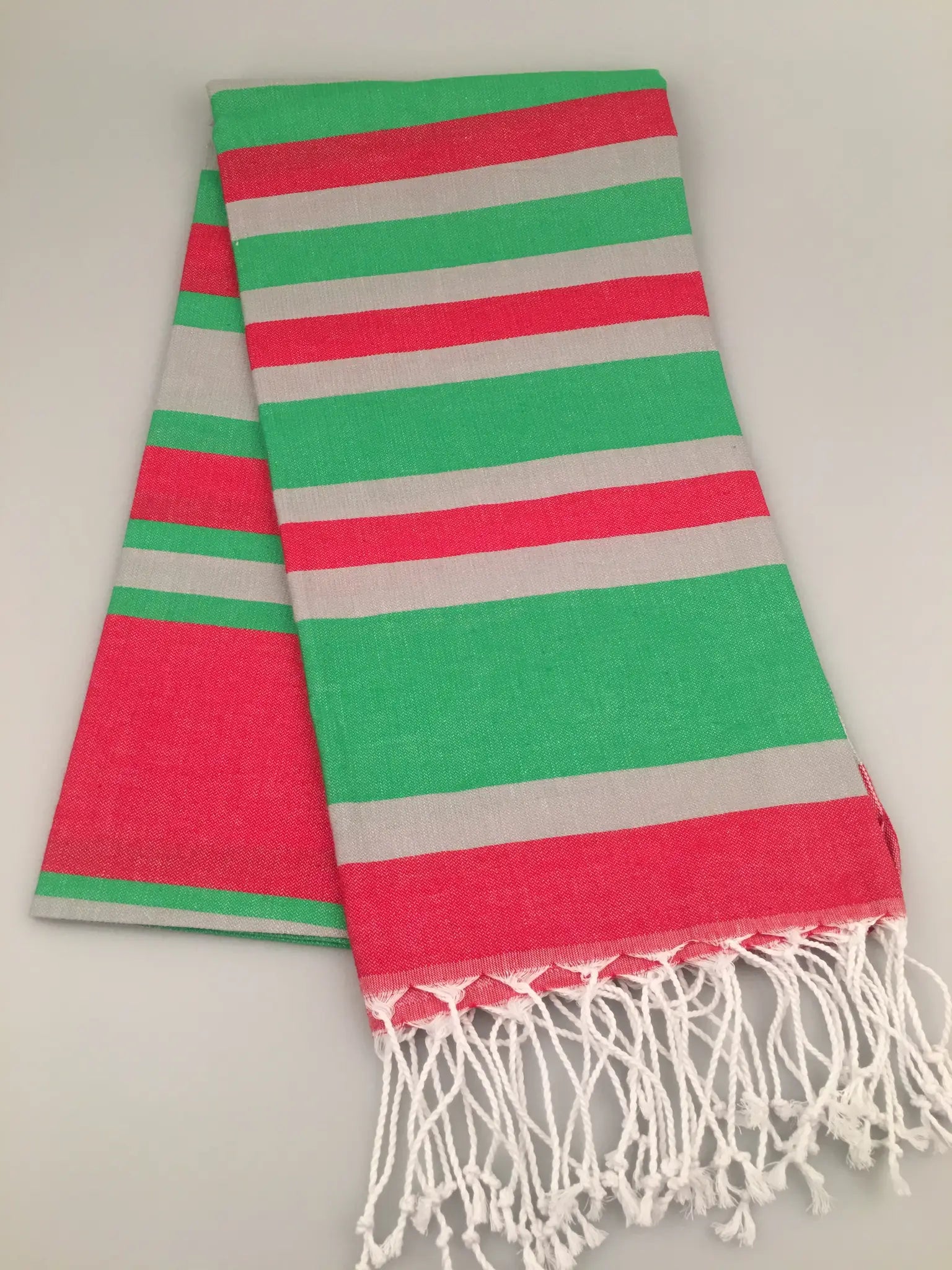 "Turquoise and coral striped Turkish towel with grey stripes and white fringe, laid flat on a light background."