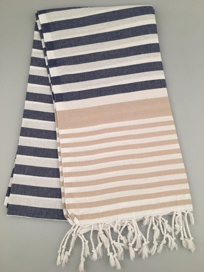 "Blue and white striped Turkish towel with beige horizontal band and fringed edges, folded flat"