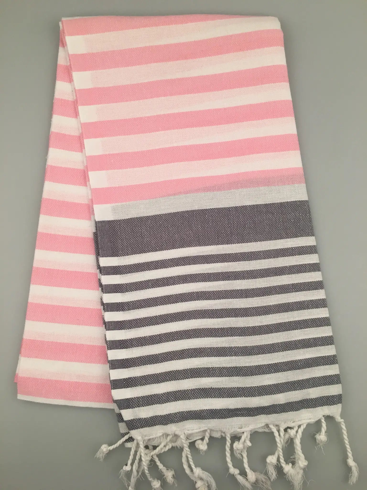 Pink and white striped Tlos Turkish Towel peshtemal with gray and white stripes at the bottom, fringed edges, laid flat.