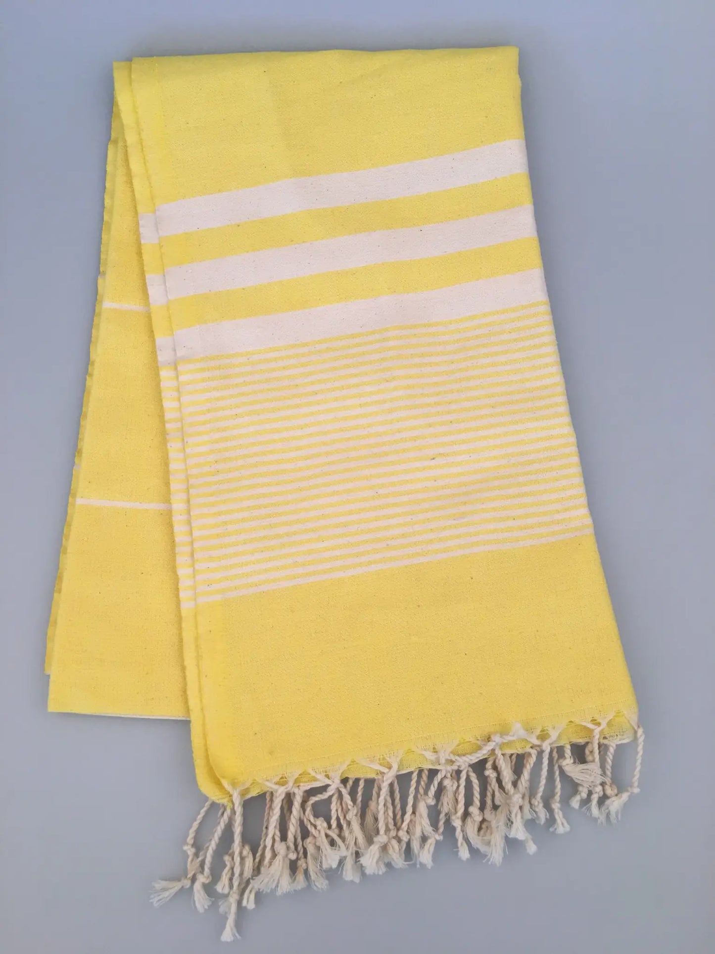 "Yellow Turkish towel peshtemal with white stripes and fringed edges, laid flat on a light gray background."