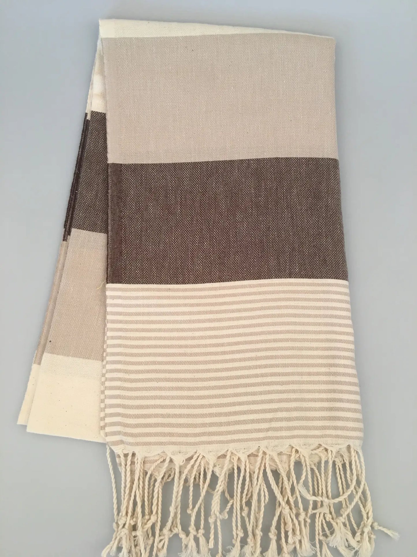 "Beige and brown striped Turkish towel with tassels, featuring a textured weave and smooth stripes."