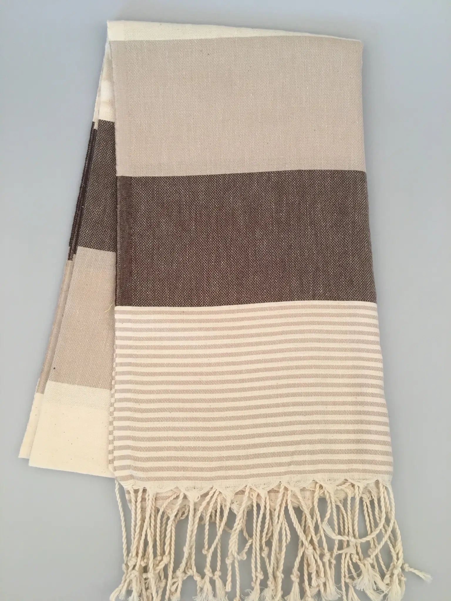 "Beige and brown striped Turkish towel with tassels, featuring a textured weave and smooth stripes."