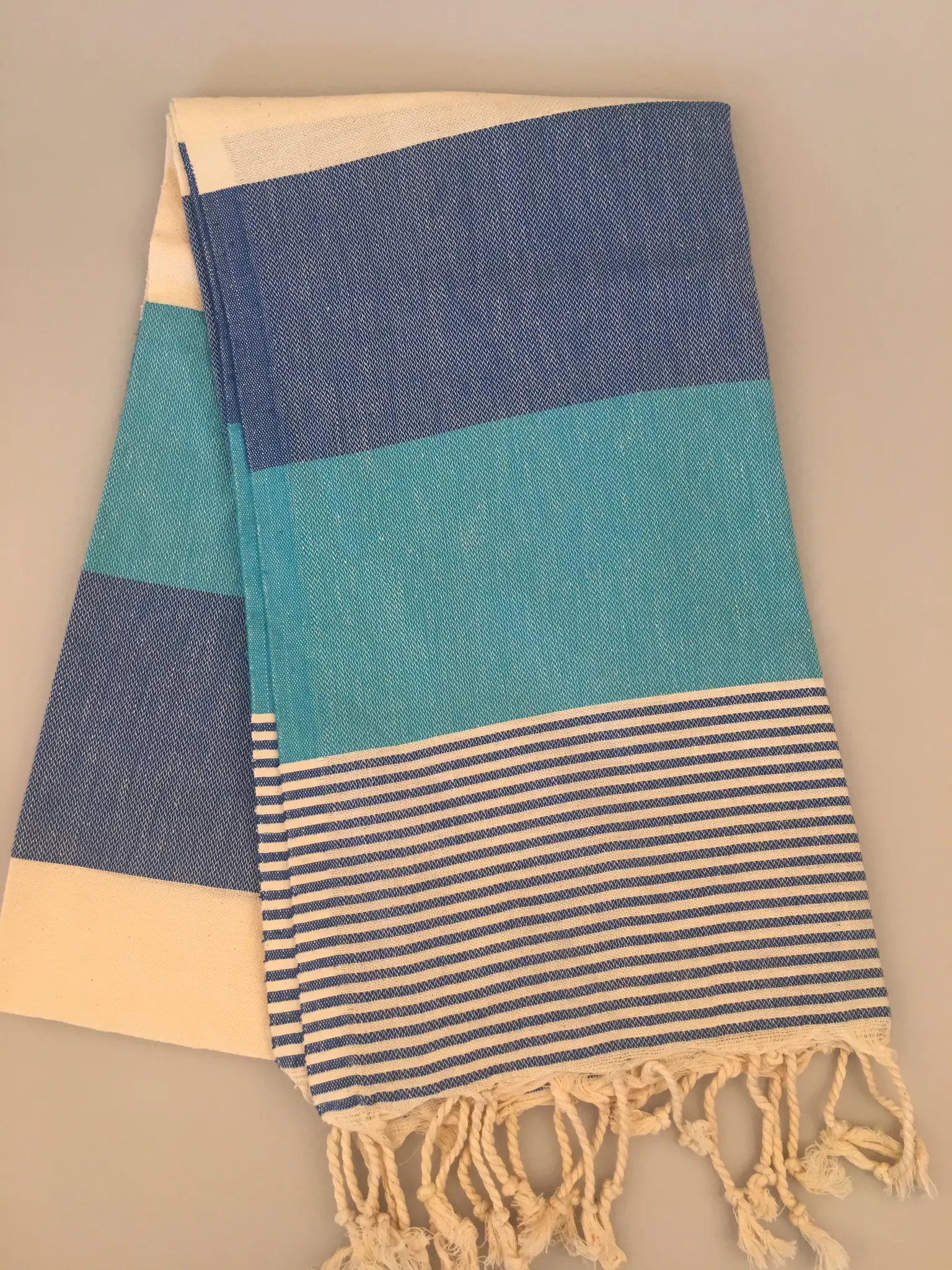 "Blue and turquoise striped Turkish towel with fringed edges, laid flat on a light background"