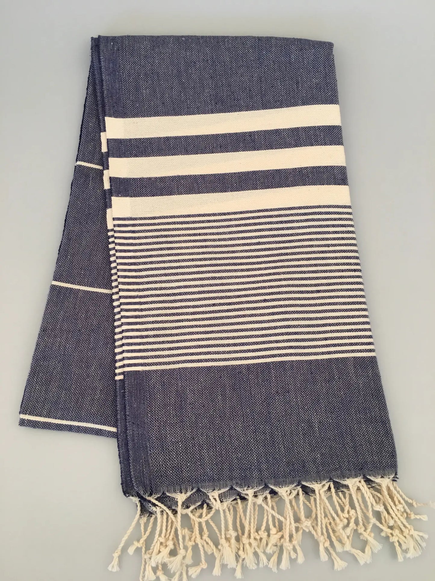 "Navy blue Turkish towel with cream stripes and fringe edges, folded with a textured weave pattern."