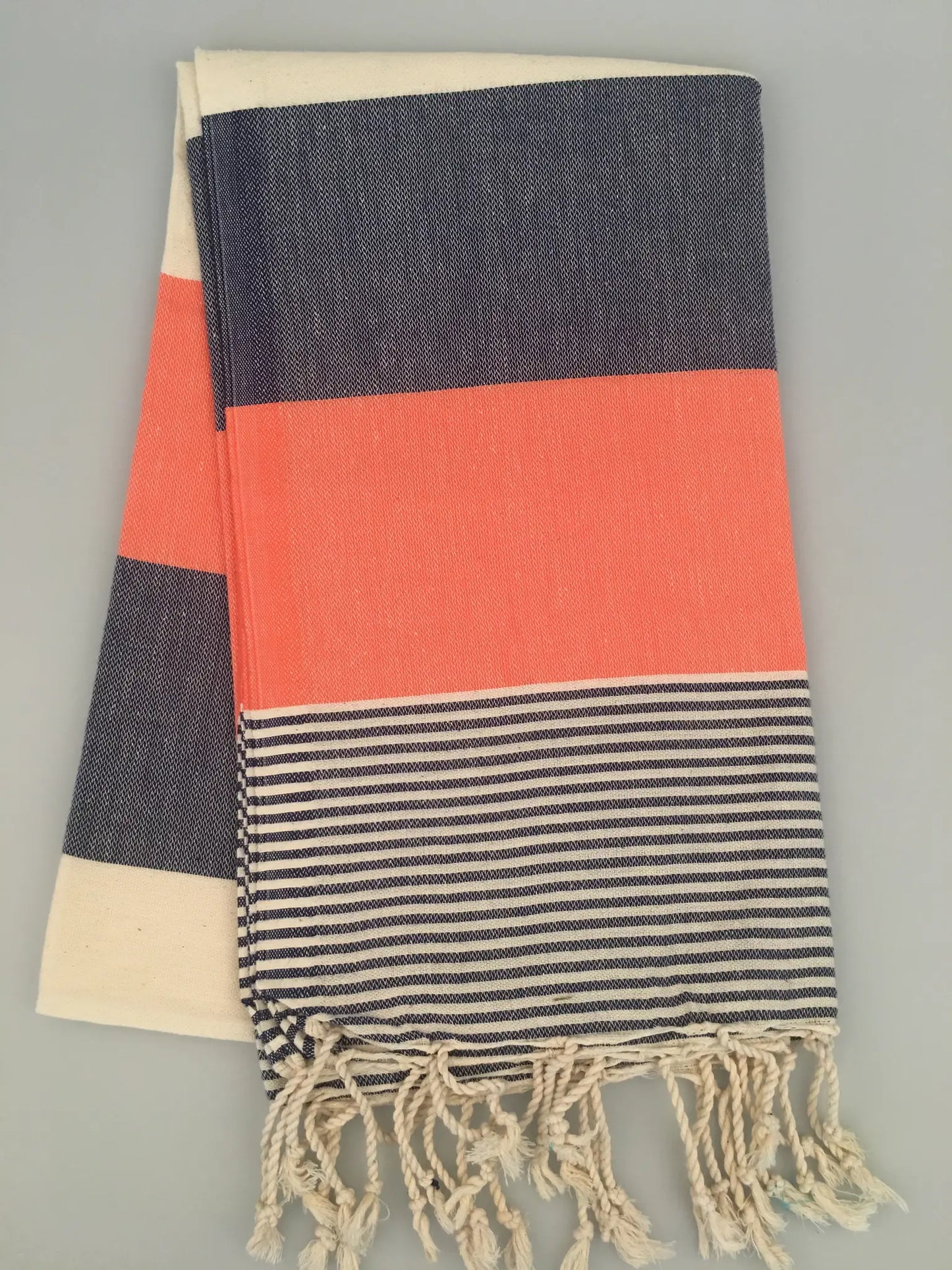 "Striped Lagina Turkish towel peshtemal with navy, coral, and cream sections, fringed edges, laid flat on a light background.