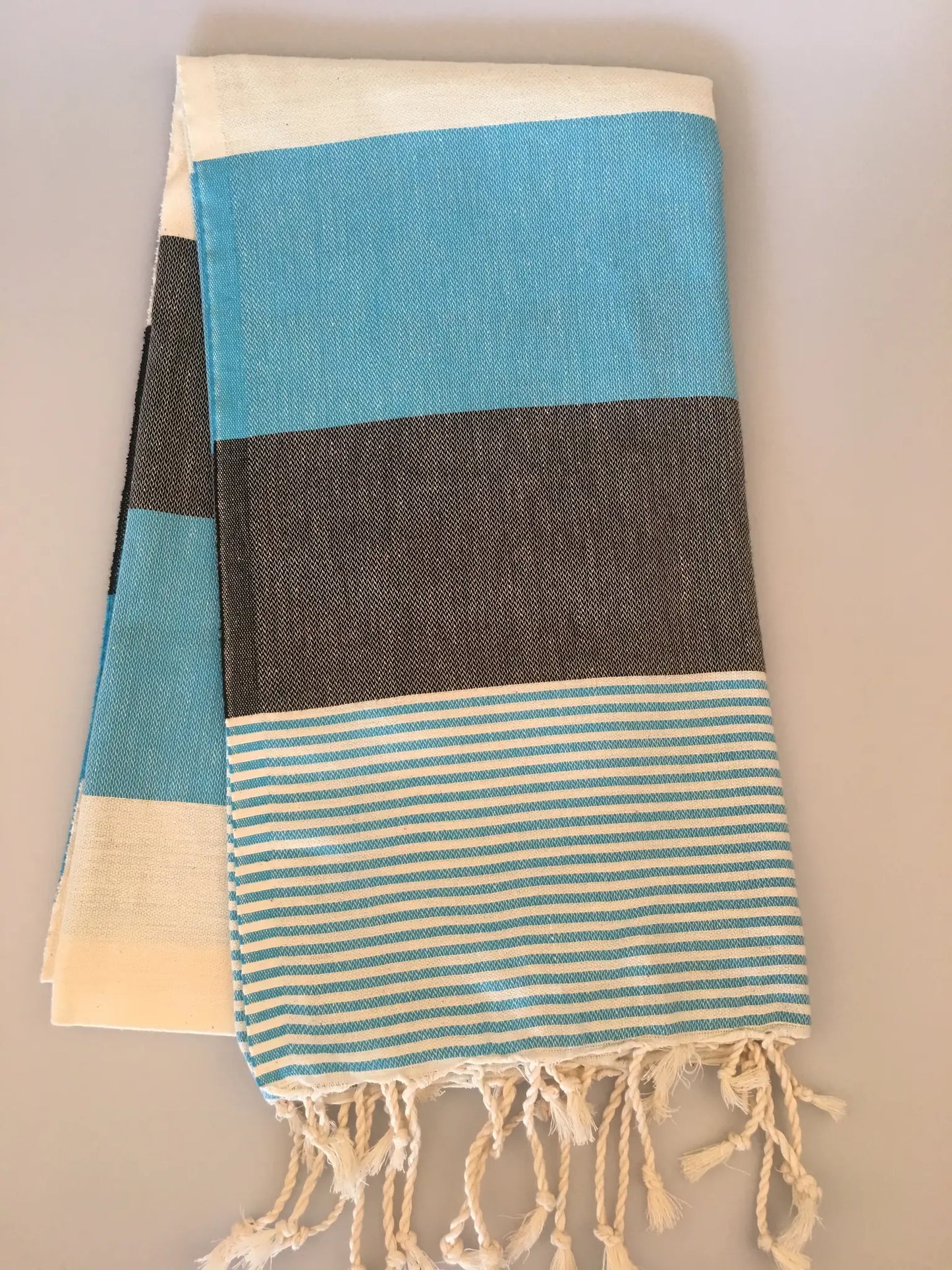 "Turquoise and gray striped Turkish towel with fringed edges, folded neatly on a light background."